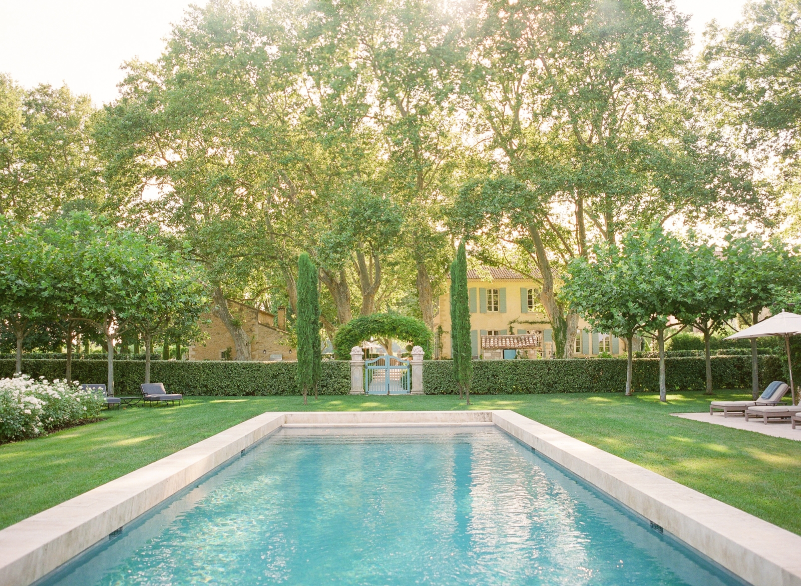 Gated pool area, lawn and patio with sun loungers and umbrellas at Mas de la Motte in Provence, France