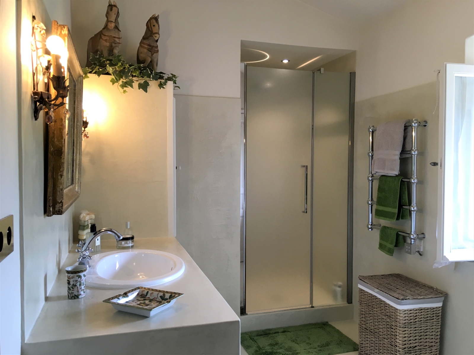 Bathroom with sink, mirror, horse statues, shower, towel rail and laundry basket at Mas des Cerisiers in Provence, France