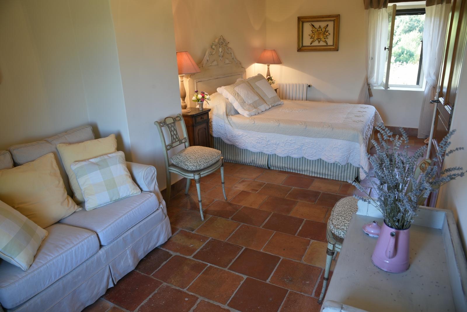 Bedroom with double bed, bedside tables, lamps, chair, flowers and sofa at Mas des Cerisiers in Provence, France