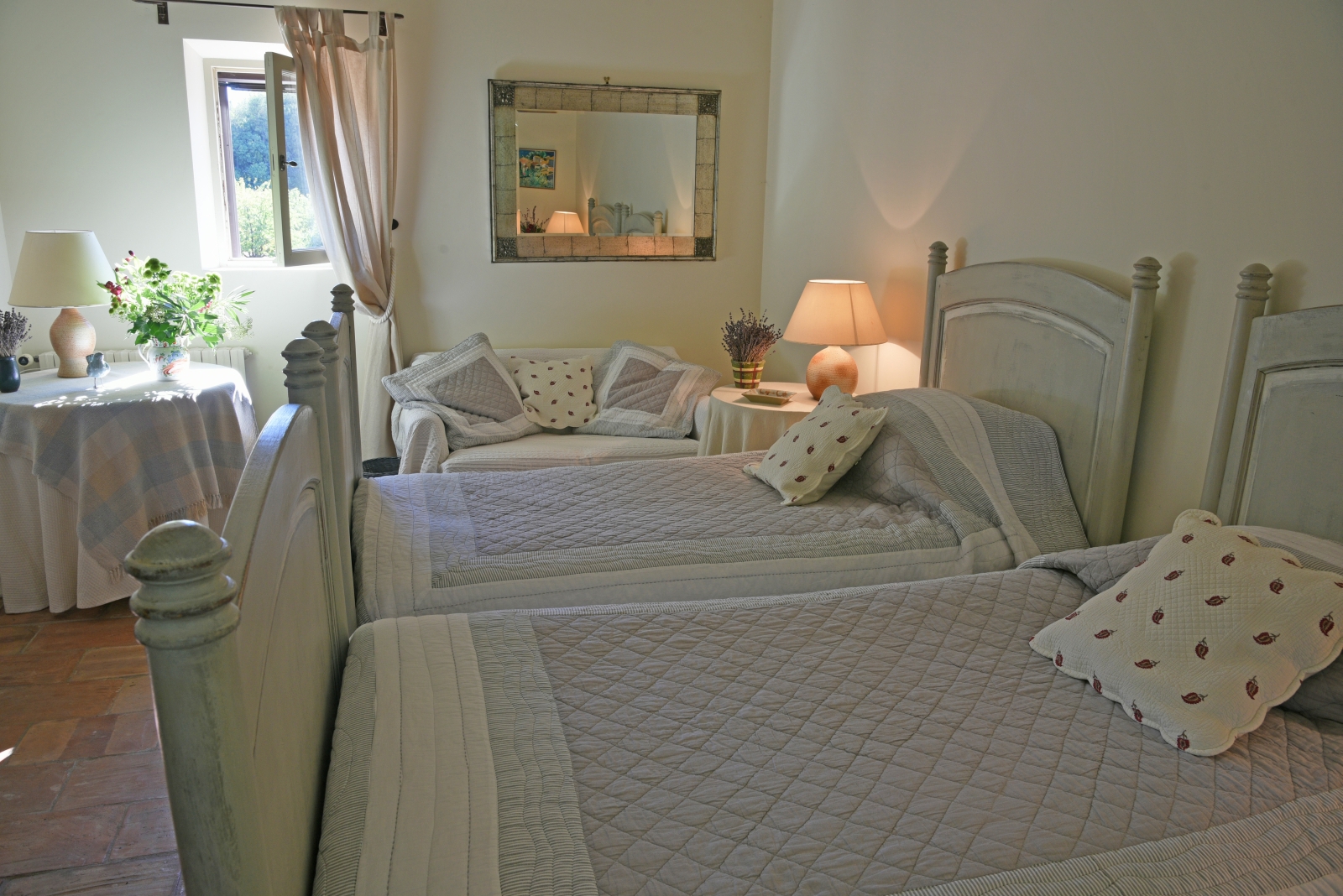 Bedroom with twin beds, tables, lamps, flowers, sofa, mirror and window at Mas des Cerisiers in Provence, France