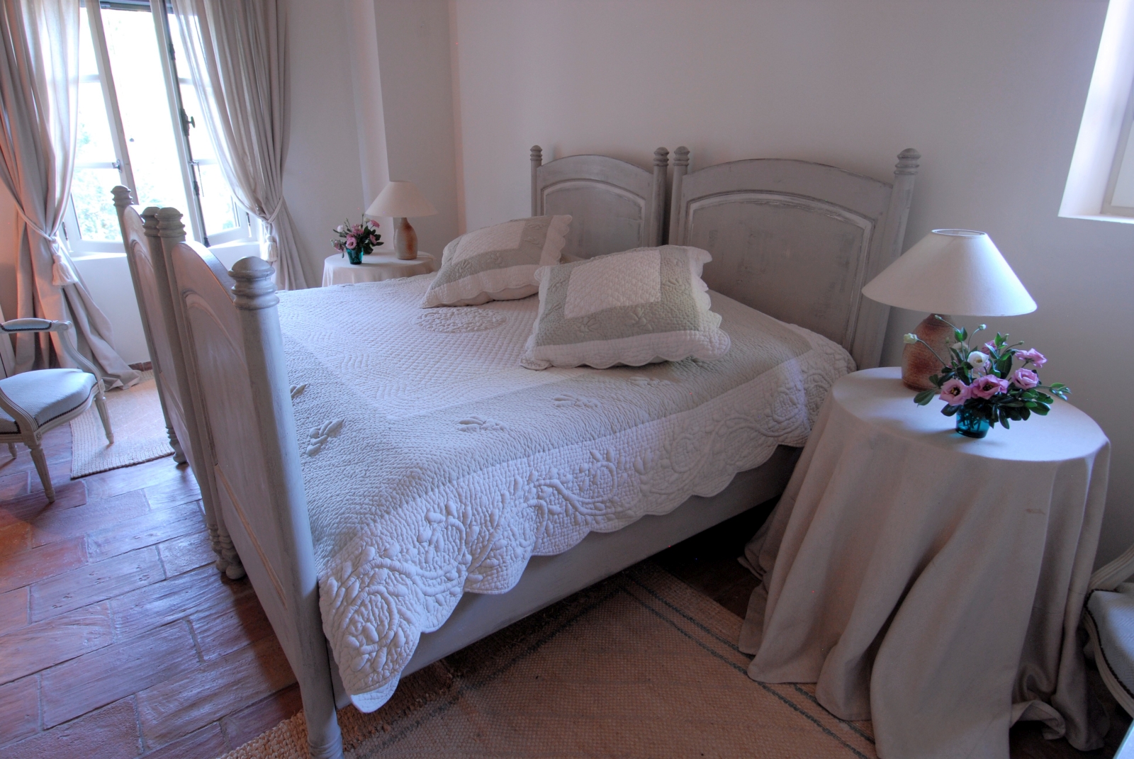 Bedroom with double bed, bedside tables, lamps, flowers and large window at Mas des Cerisiers in Provence, France
