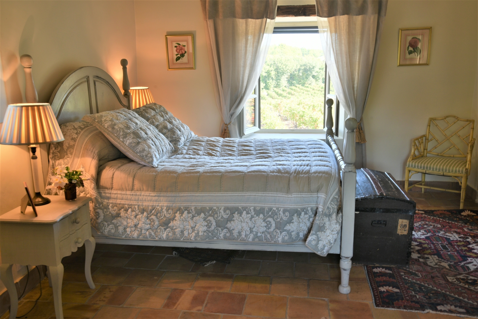 Bedroom with double bed, bedside table, lamp, chest, chair, picture frames & window at Mas des Cerisiers in Provence, France