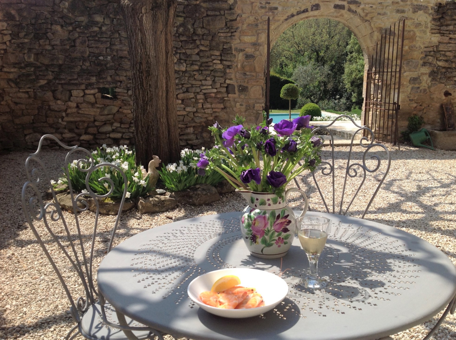 Courtyard with table chairs, flowers, wine glass and gates to pool area at Mas des Cerisiers in Provence, France
