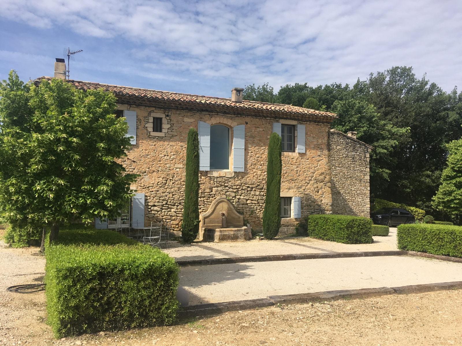 Façade of villa, fountain, trees, hedges and boules court at Mas des Cerisiers in Provence, France
