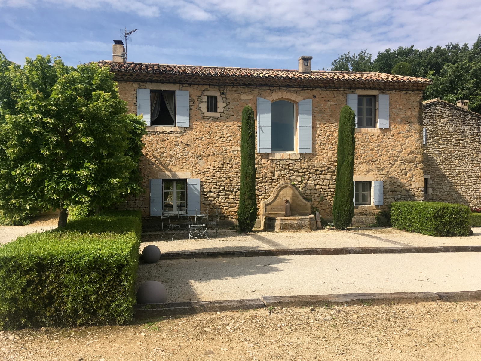 Facade, trees, hedges, boules court and dining table at Mas des Cerisiers in Provence, France