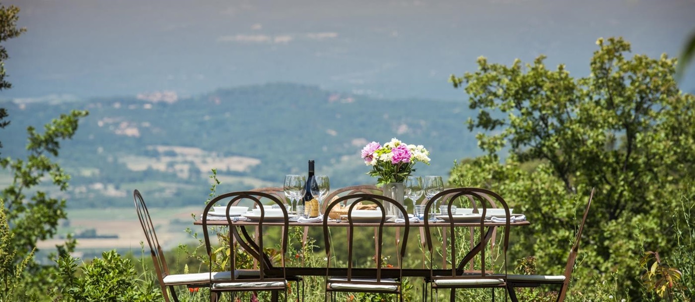 Outdoor dining area with set table, chairs, flowers and countryside view at Mas du Buis in Provence, France