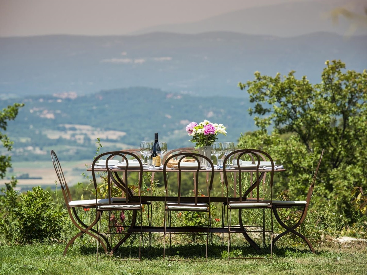 Outdoor dining area with set table, chairs, flowers and countryside view at Mas du Buis in Provence, France