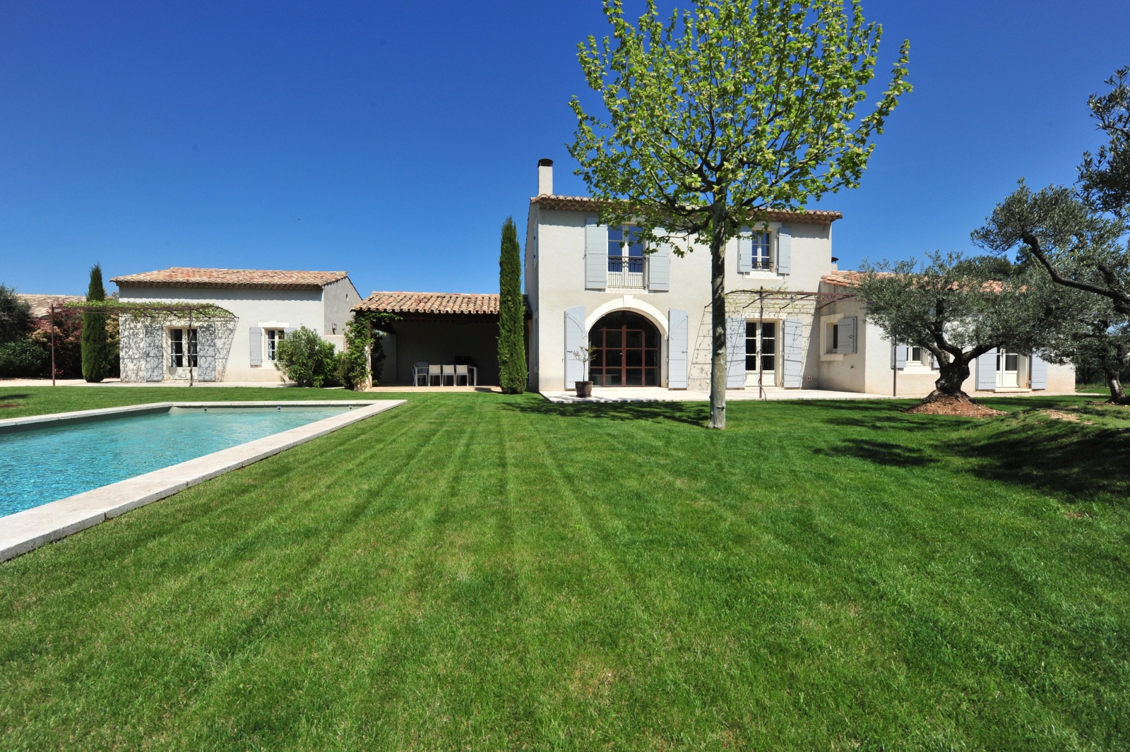 Green lawn with front of villa and side of pool at Mas Eygalieres in Provence