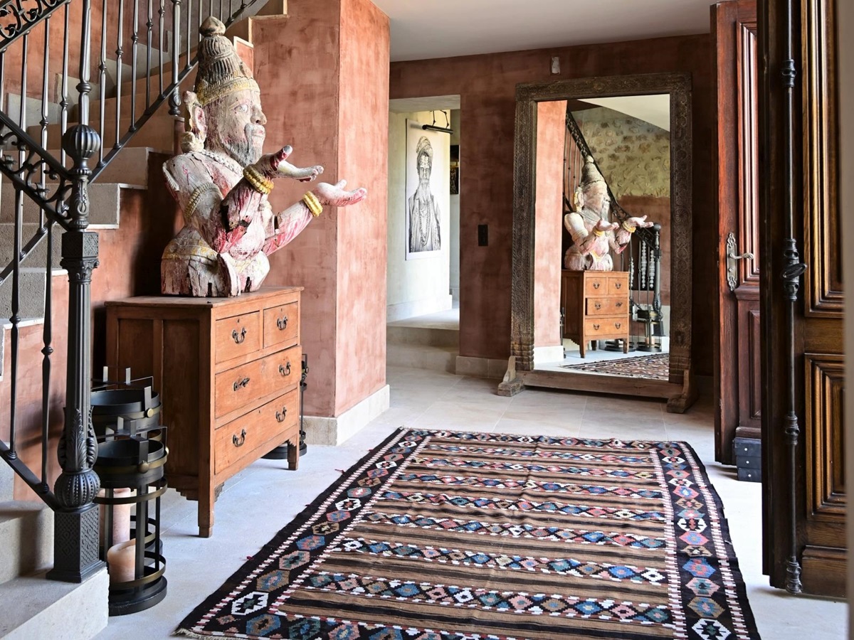 Hallway with buddha statue, drawers, patterned rug, candles, large mirror and staircase at Villa Athena in Provence, France
