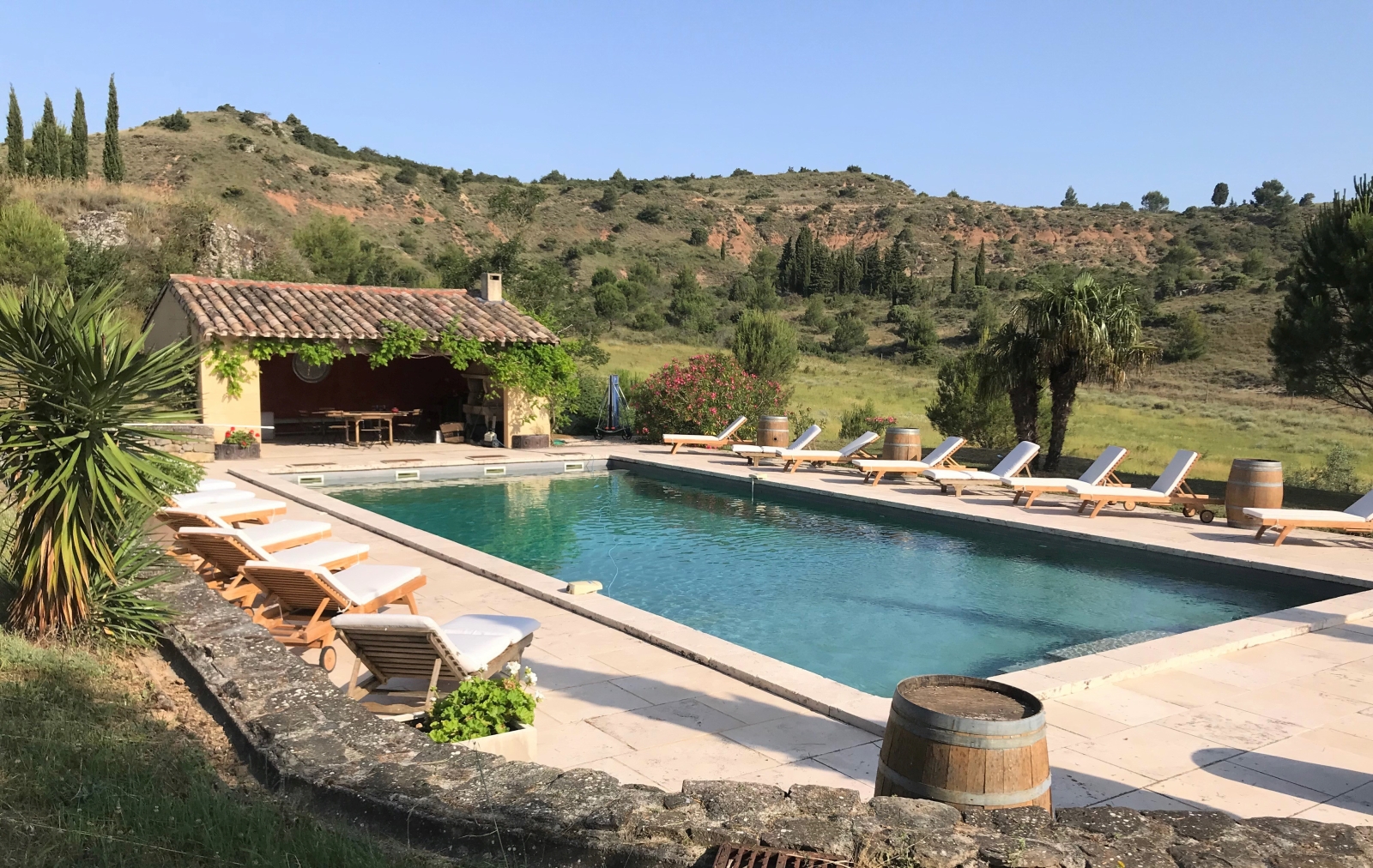Pool and patio area with sun loungers, flowers and covered dining area at Domaine de Corbieres in South West France