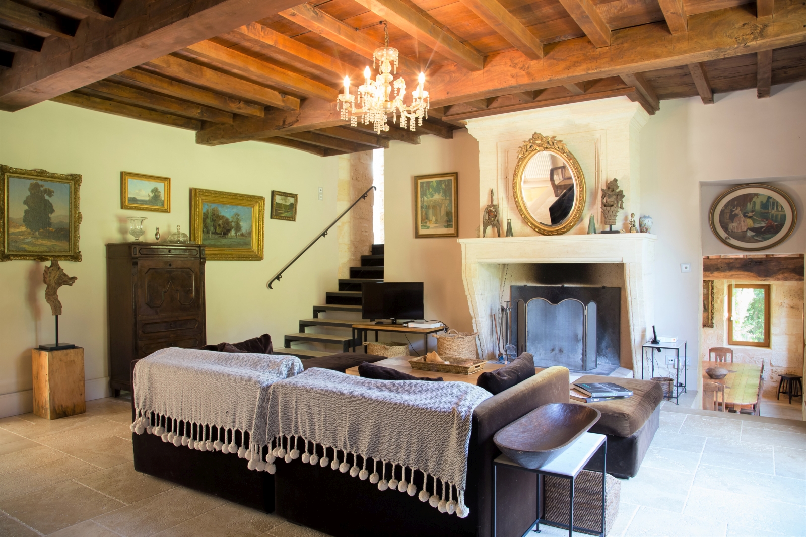 Living room with sofa, coffee table, TV, fireplace, chandelier and paintings at La Colline Bleue in South West France