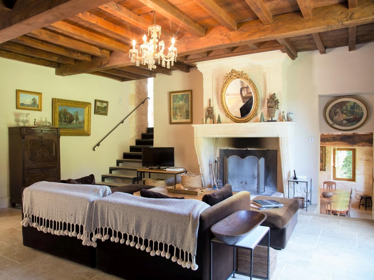 Living room with sofa, coffee table, TV, fireplace, chandelier and paintings at La Colline Bleue in South West France