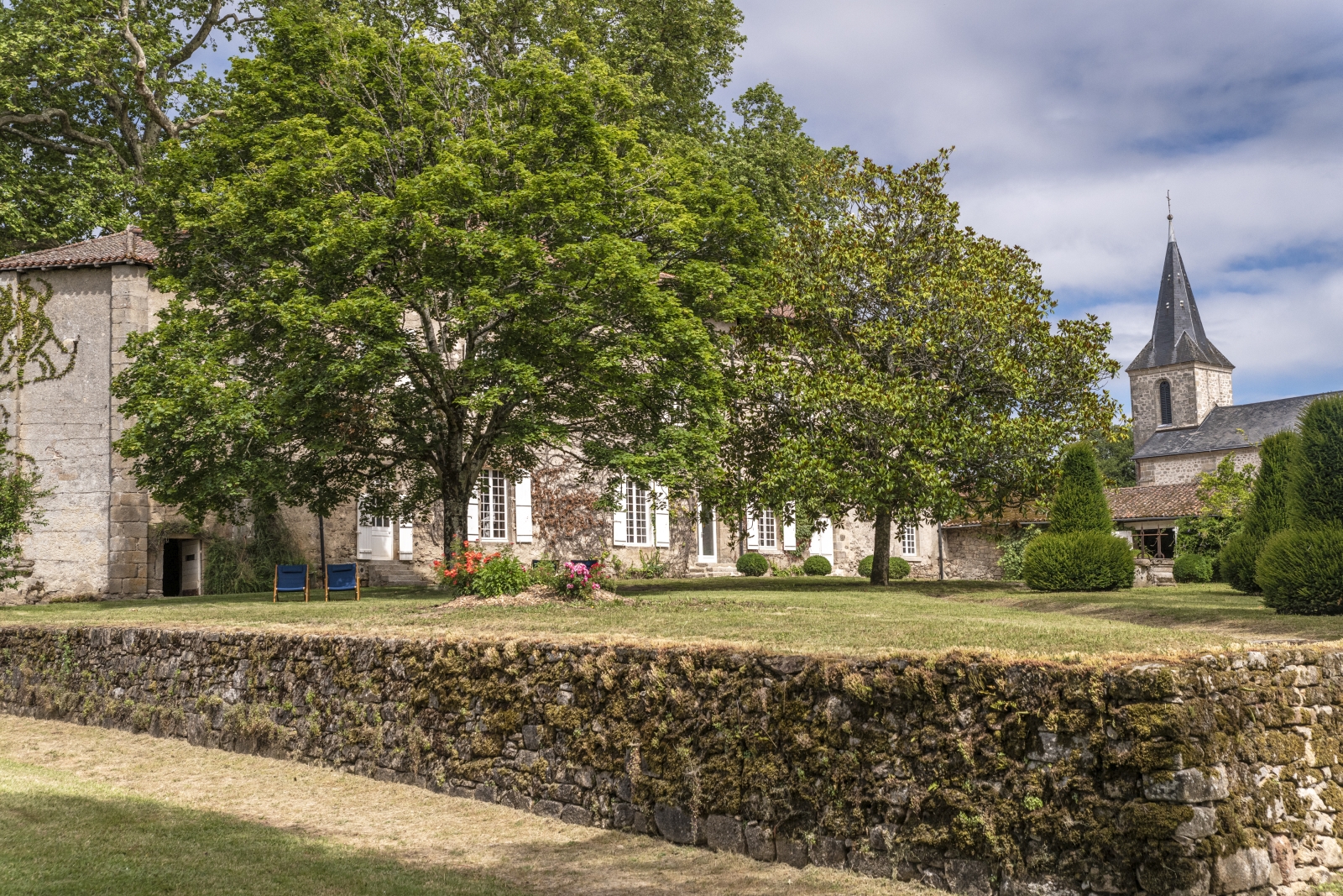 Garden of property with stone wall and view of church at Le Clos Colombier in France