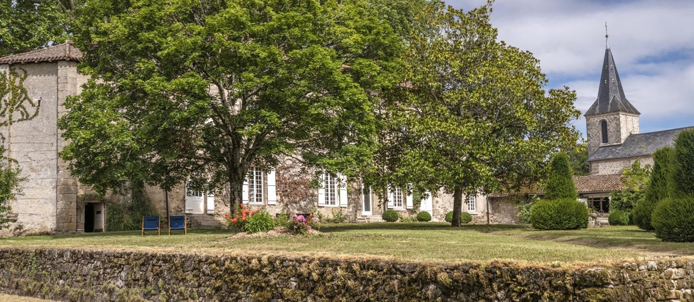 Garden of property with stone wall and view of church at Le Clos Colombier in France