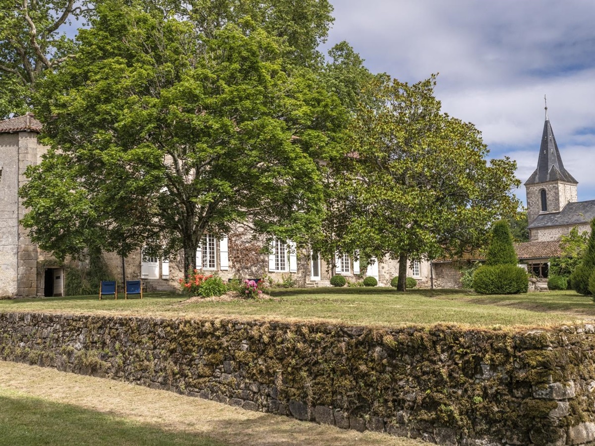 Garden of property with stone wall and view of church at Le Clos Colombier in France