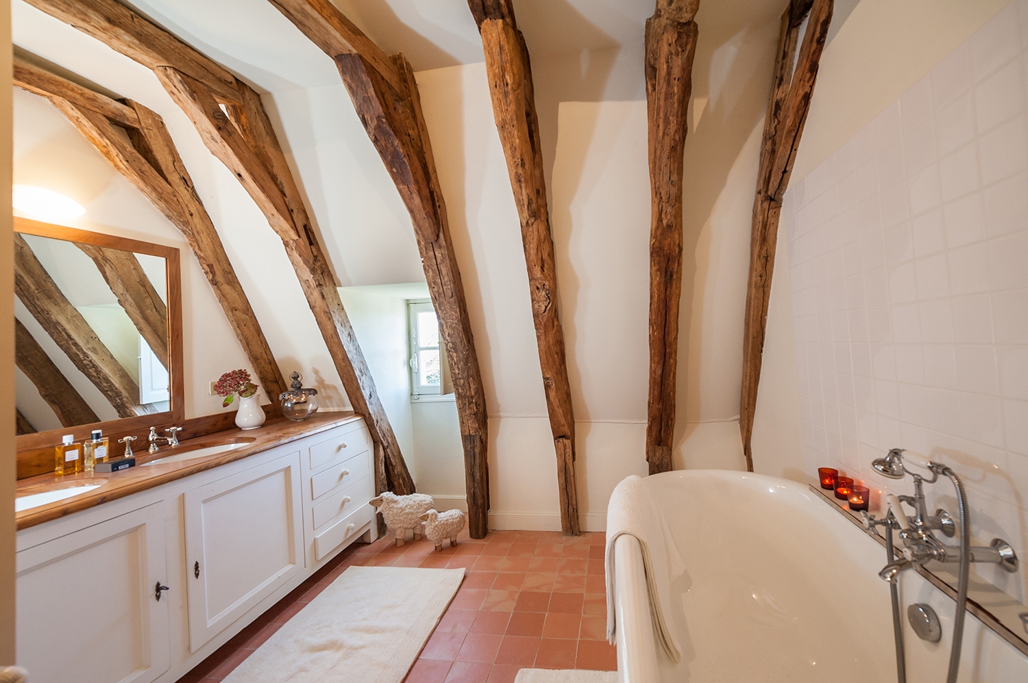 Bathroom with bath, candles, double sinks, large mirror, flowers and ceiling beams at Maison de Cales in South West France