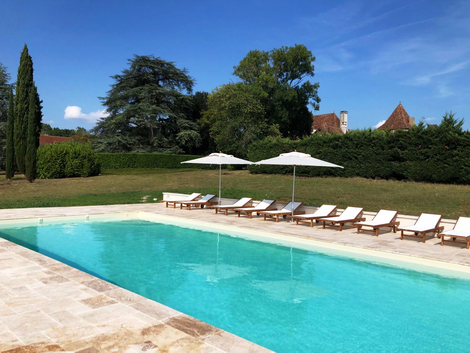 swimming pool with white sunbeds and umberllas at villa maison de cales in south west france
