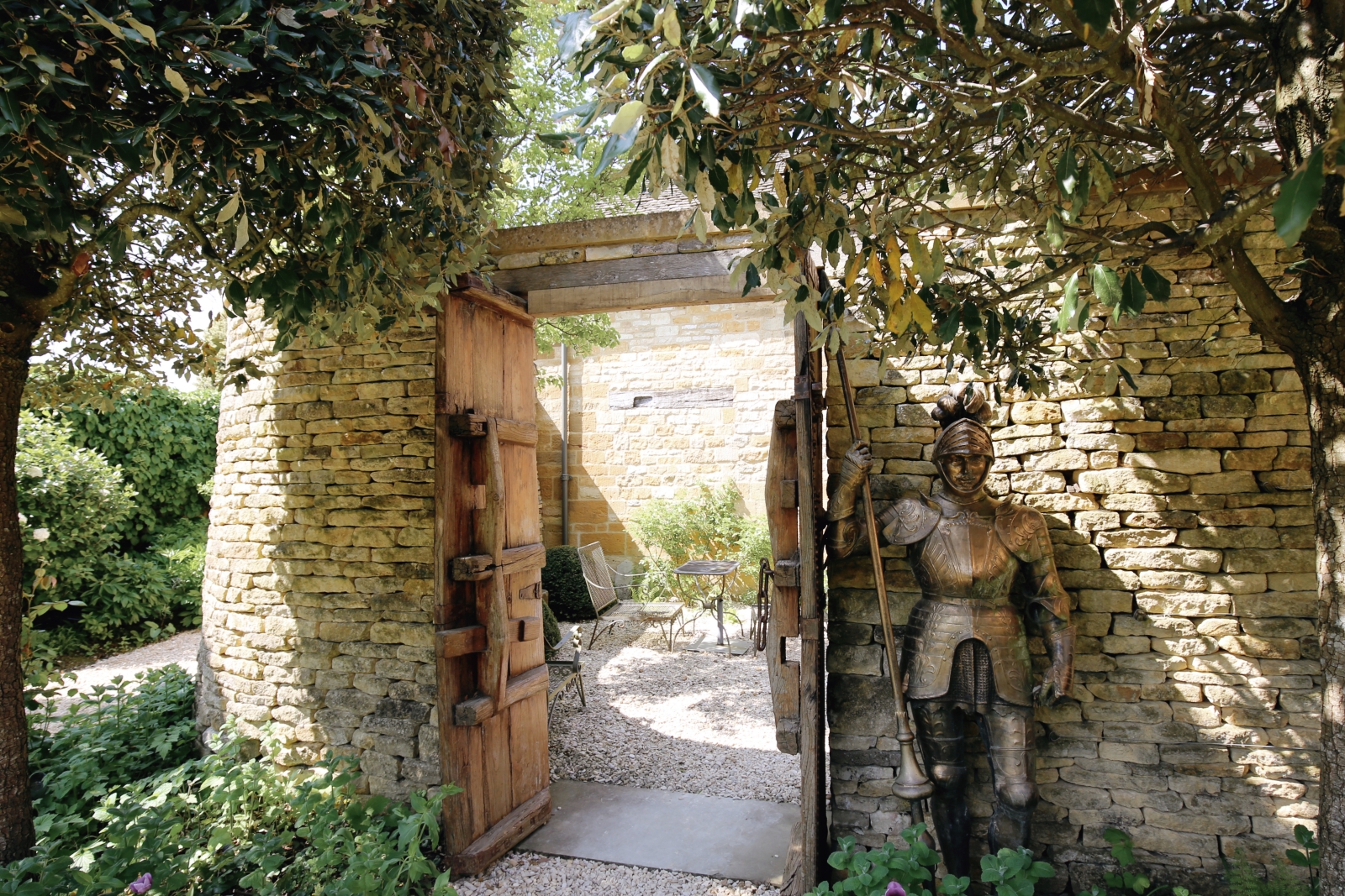 Knight statue beside a doorway leading to a walled outdoor seating area at Temple Guiting Barn, luxury villa in the Cotswolds, England