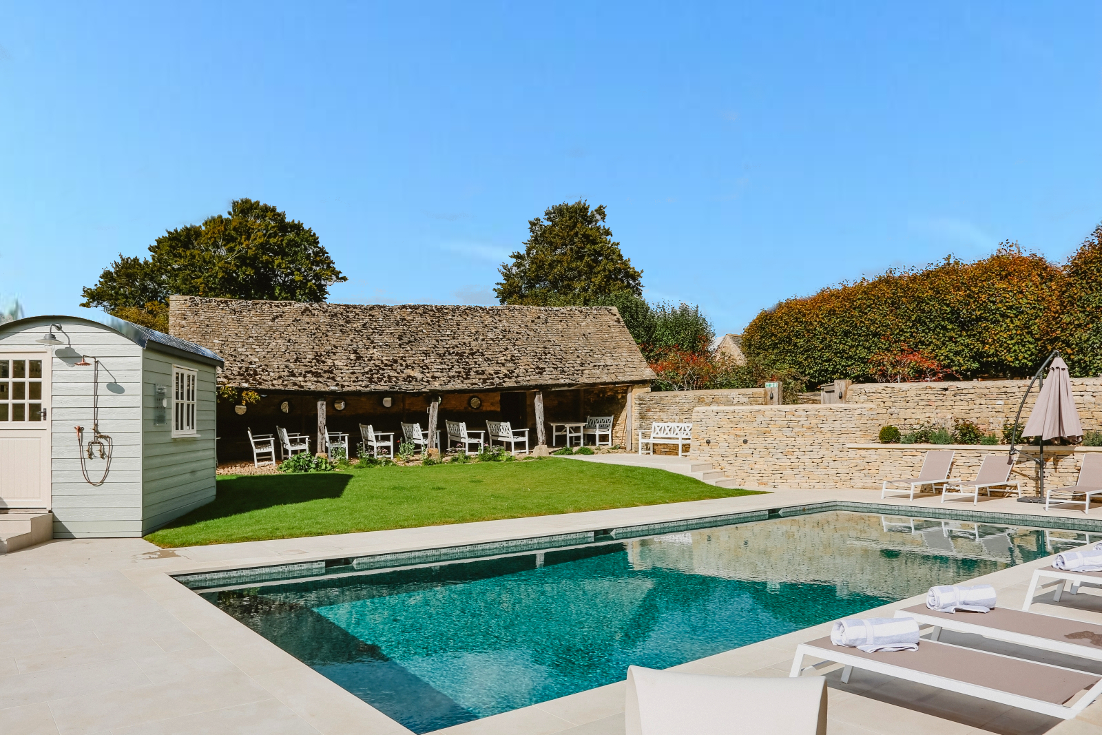 Pool and loungers with an outdoor shower at Temple Guiting Barn, luxury villa in the Cotswolds, England