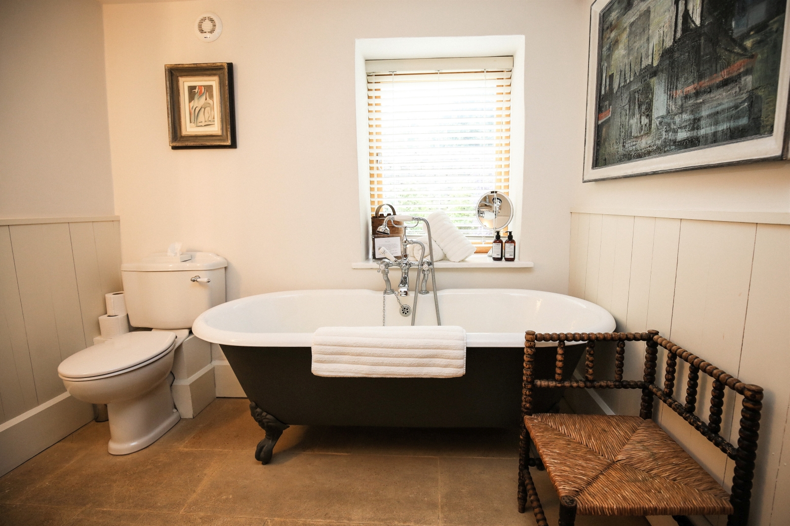 Bathroom with chair, paintings, bath and toilet at Temple Guiting Barn in the Cotswolds, England