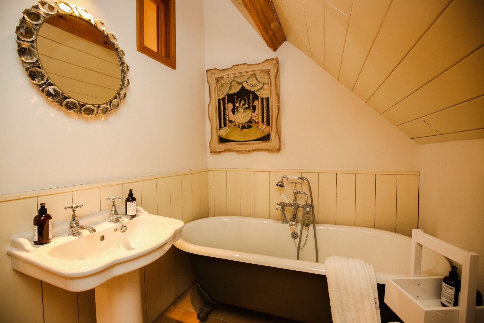 Bathroom with caddy, bath, painting, sink and mirror at Temple Guiting Barn in the Cotswolds, England