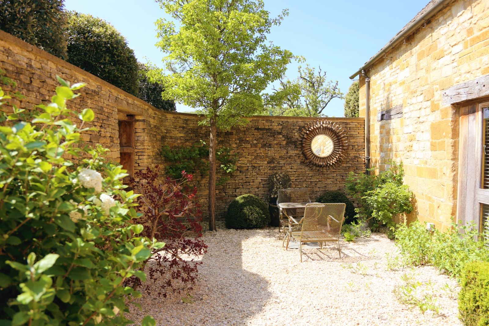 Courtyard with plants, flowers, tree and table and chairs at Temple Guiting Barn in the Cotswolds, England