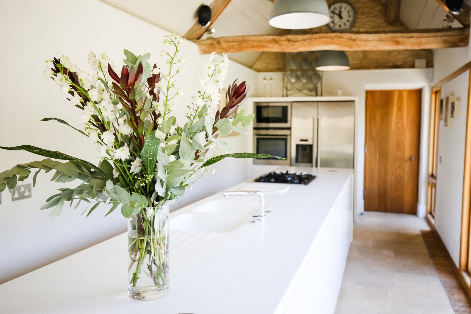 Kitchen with flowers, sink, hob, fridge and oven at Temple Guiting Barn in the Cotswolds, England
