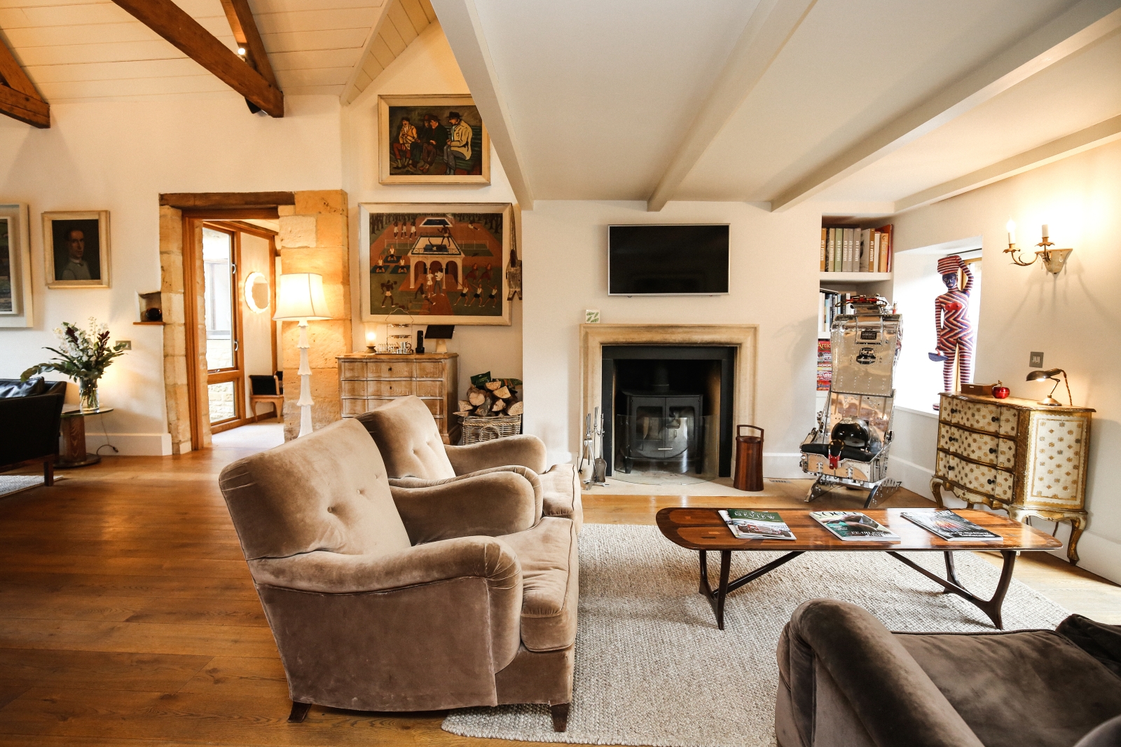 Living room with armchairs, coffee table, cabinets, fireplace and paintings at Temple Guiting Barn in the Cotswolds, England