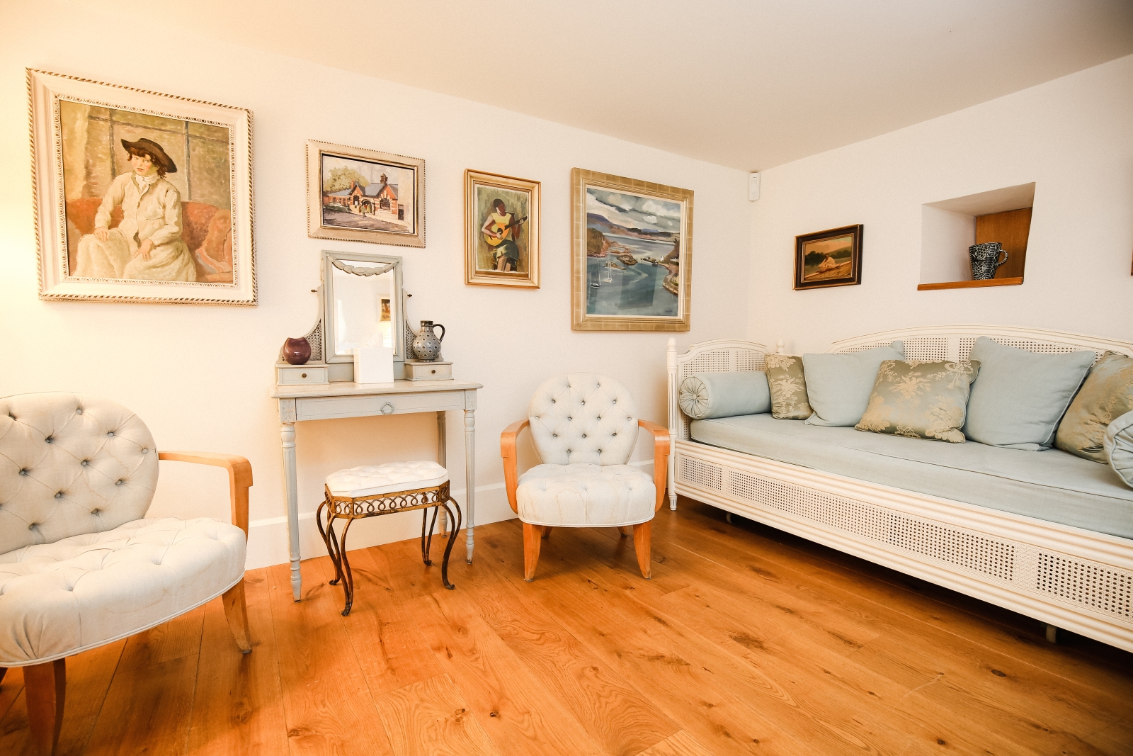 Bedroom with sofa, armchairs, dressing table, stool and paintings at The Estate at Temple Guiting in the Cotswolds, England