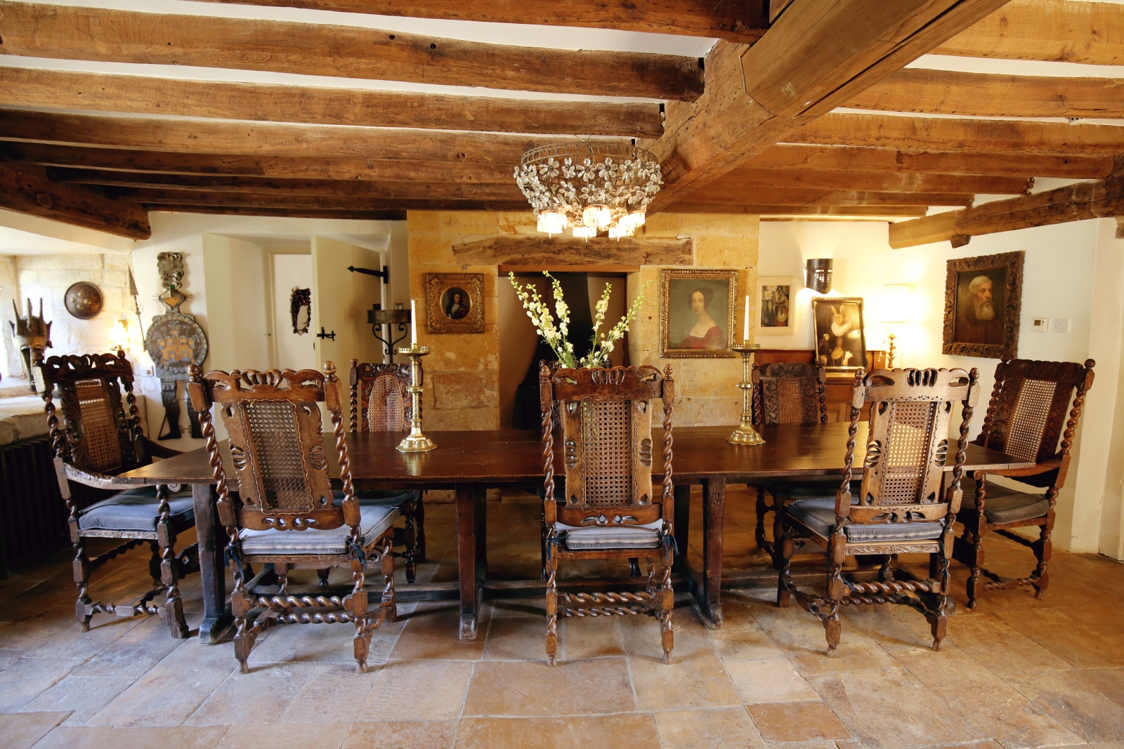 Dining room with long wooden table, chairs, paintings & chandelier at The Estate at Temple Guiting in the Cotswolds, England