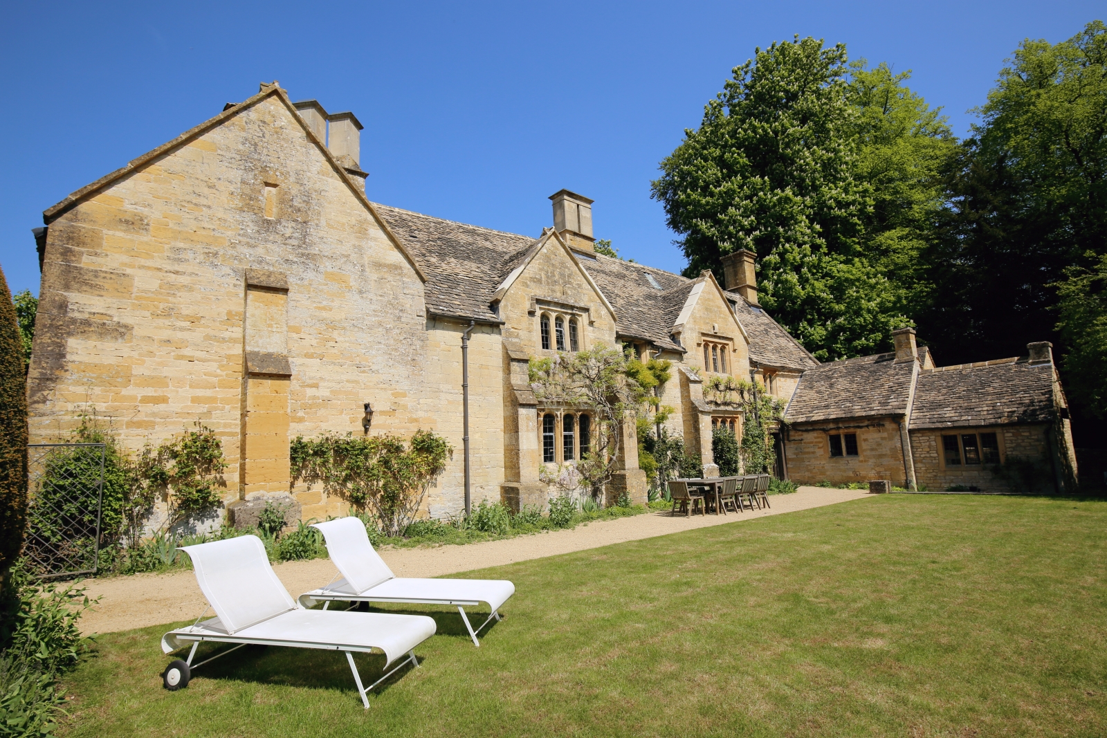 Cotswold stone back of villa with table, chairs and sun loungers at The Estate at Temple Guiting in the Cotswolds, England