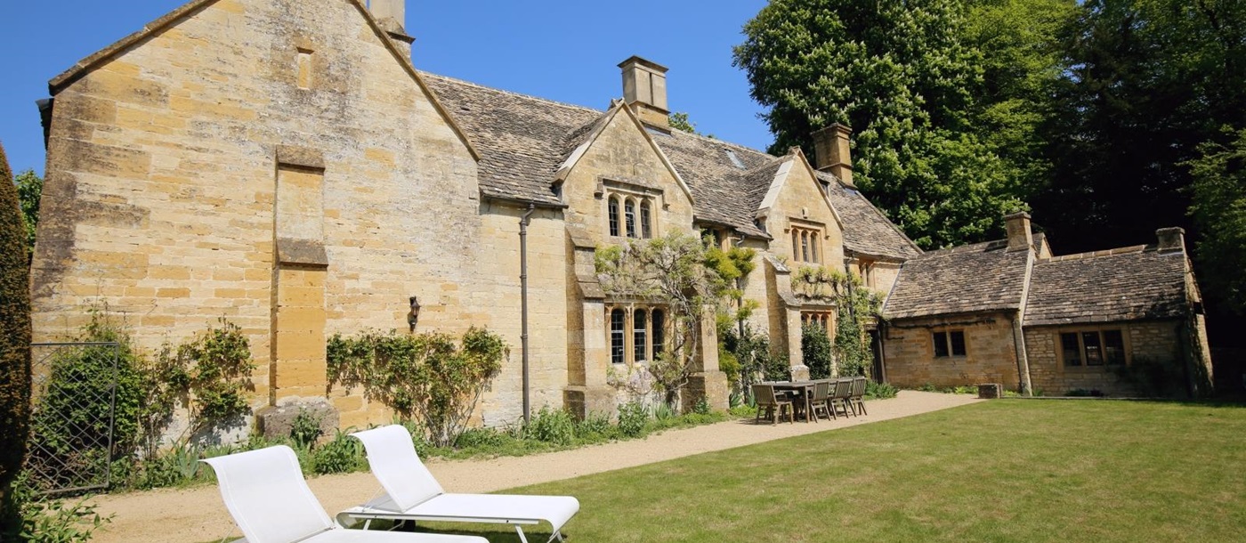 Cotswold stone back of villa with table, chairs and sun loungers at The Estate at Temple Guiting in the Cotswolds, England