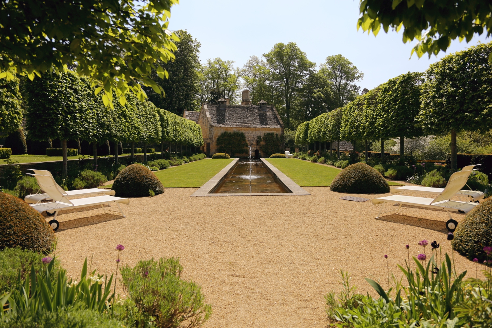 Garden with flowers, sun loungers, hedges, lawn, pond and trees at The Estate at Temple Guiting in the Cotswolds, England
