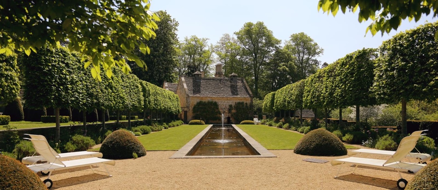 Garden with flowers, sun loungers, hedges, lawn, pond and trees at The Estate at Temple Guiting in the Cotswolds, England