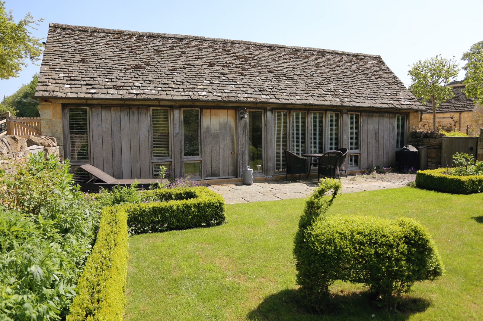 Exterior view of Cow Byre guest house and lawn with pig shape hedge at The Estate at Temple Guiting in the Cotswolds, England