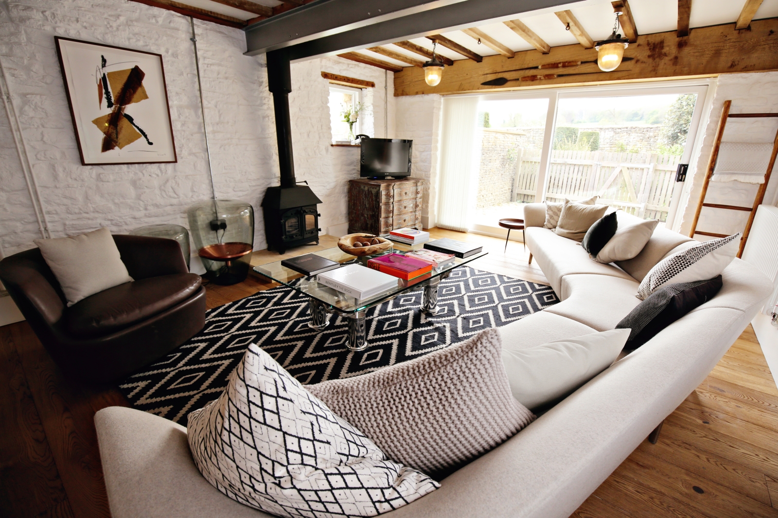 Living room with long sofa, armchair, coffee table, TV & fireplace at The Estate at Temple Guiting in the Cotswolds, England