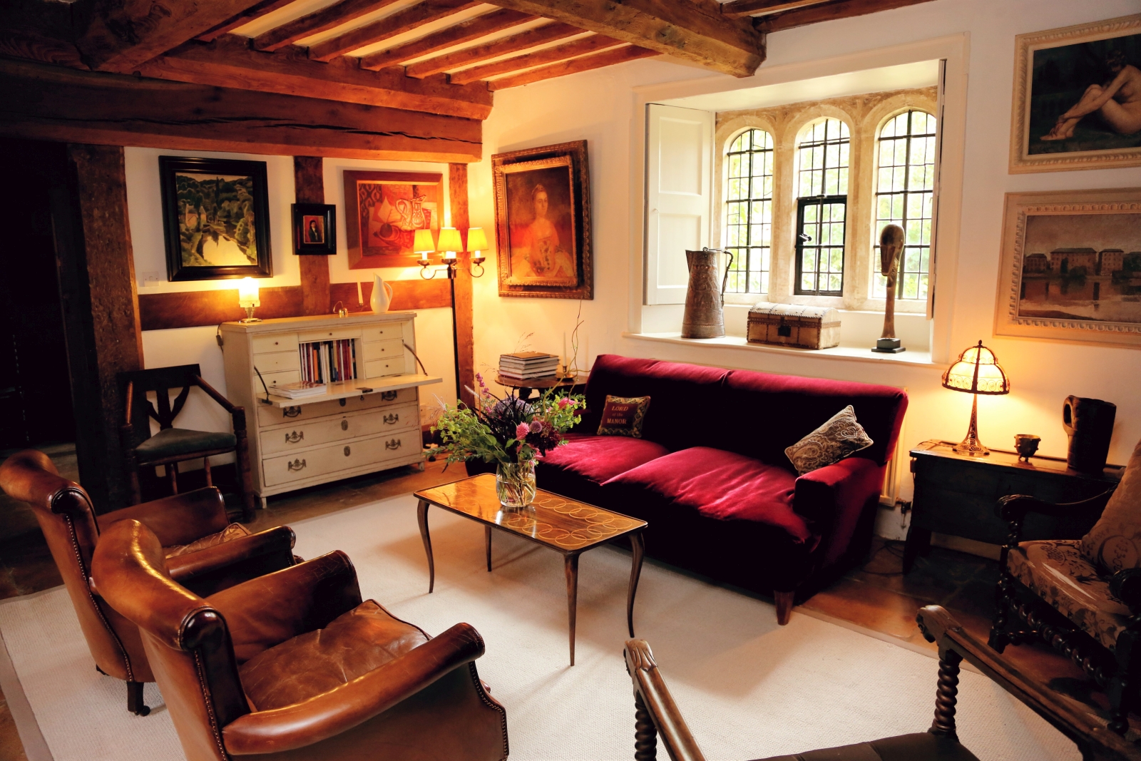 Living room with sofa, armchairs, table, paintings and cabinet at The Estate at Temple Guiting in the Cotswolds, England