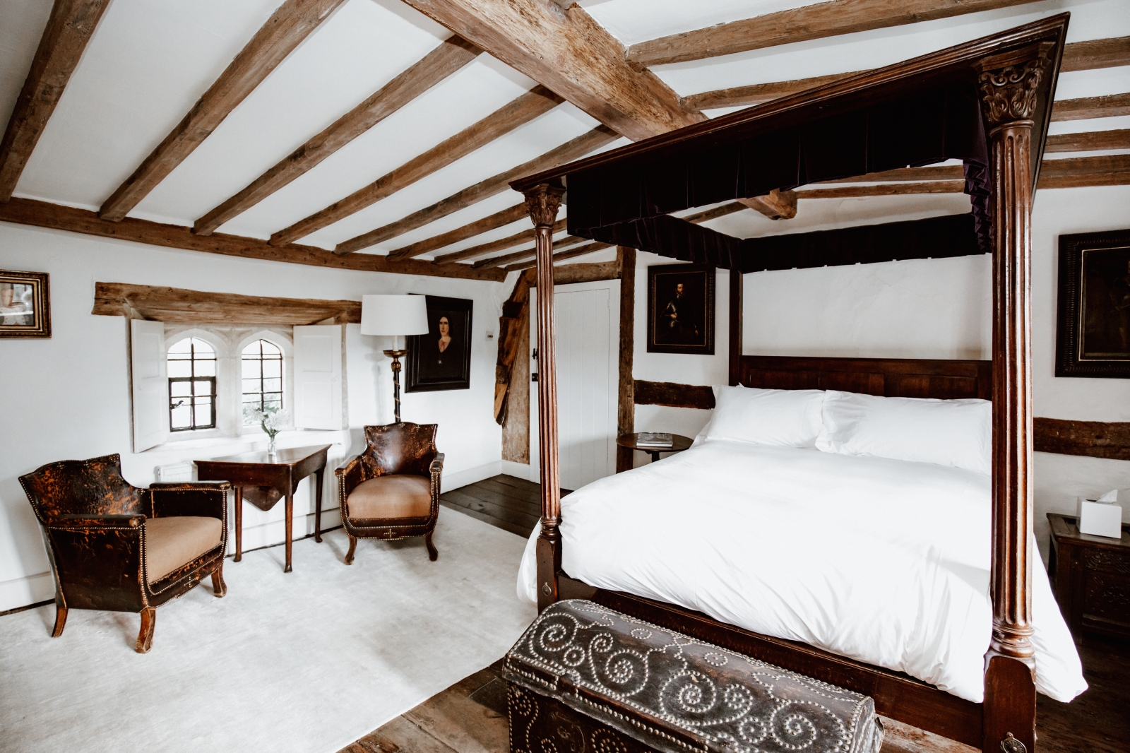 Double bedroom with four poster bed and separate seating area as well as exposed wooden beams at luxury villa Temple Guiting Manor in the Cotswolds, United Kingdom