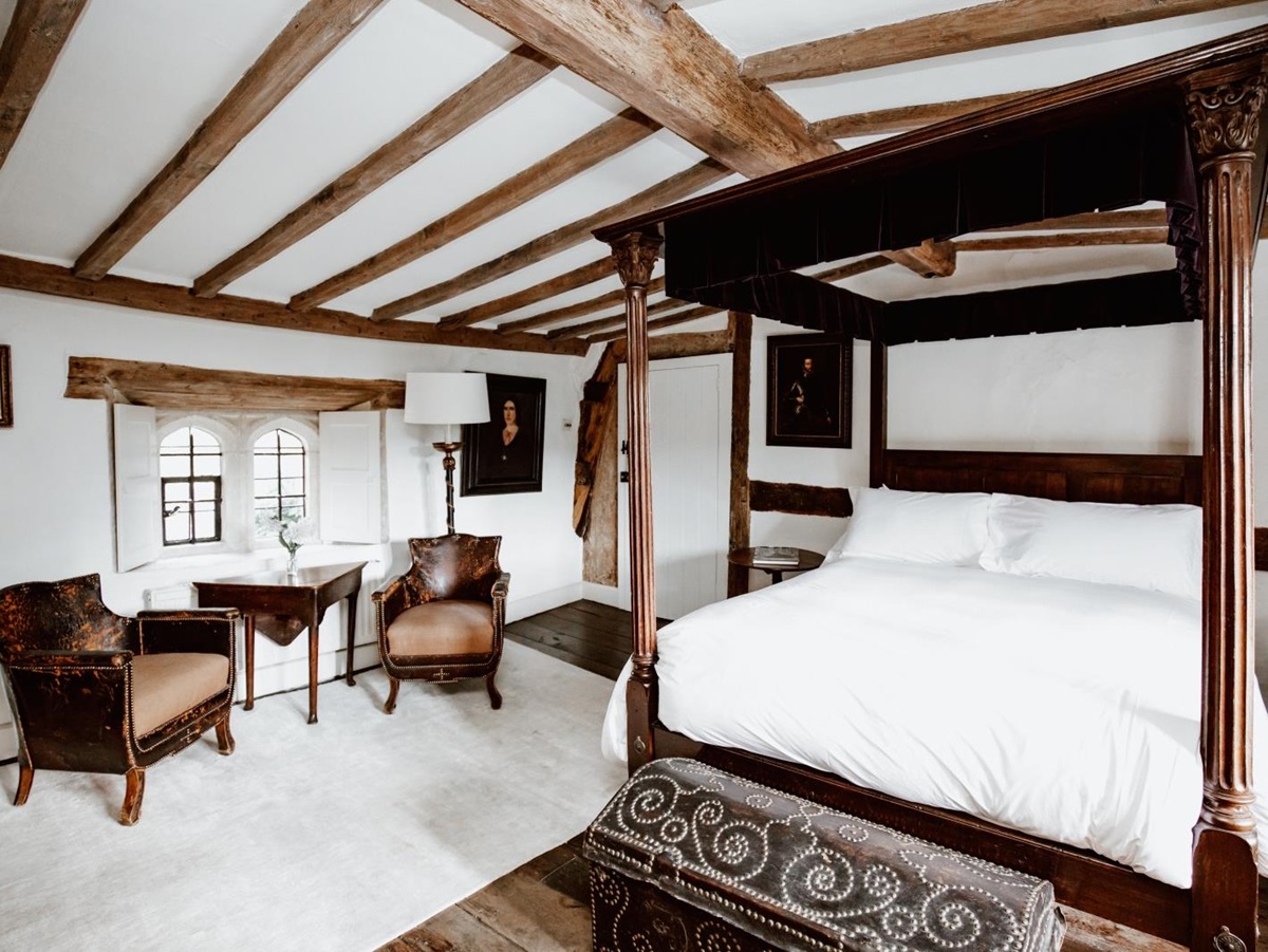 Double bedroom with four poster bed and separate seating area as well as exposed wooden beams at luxury villa Temple Guiting Manor in the Cotswolds, United Kingdom