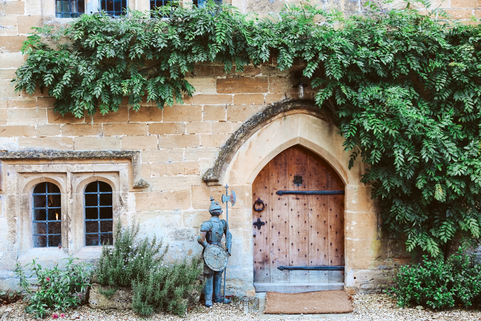 Medieval door into the villa, with decorative knight statue and ivy at English luxury villa Temple Guiting Manor