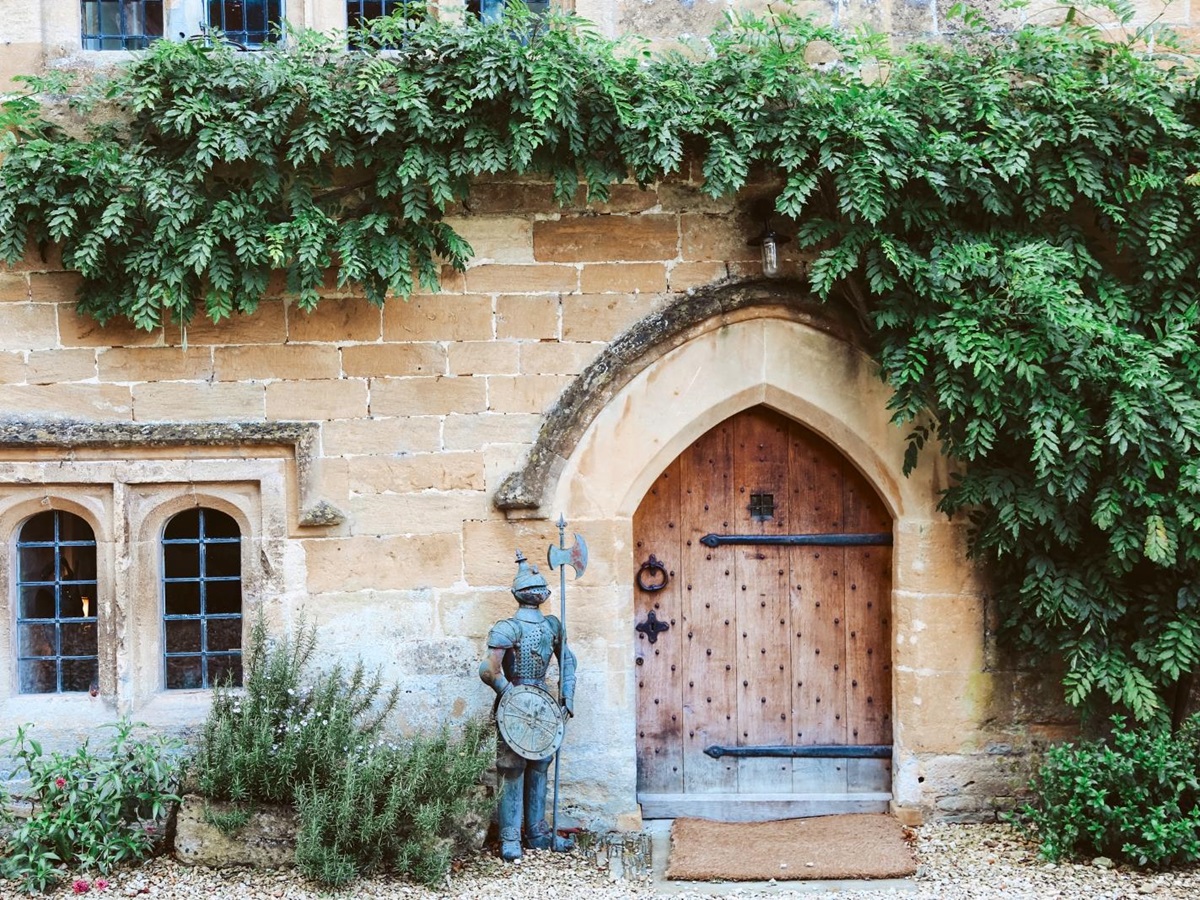 Medieval door into the villa, with decorative knight statue and ivy at English luxury villa Temple Guiting Manor