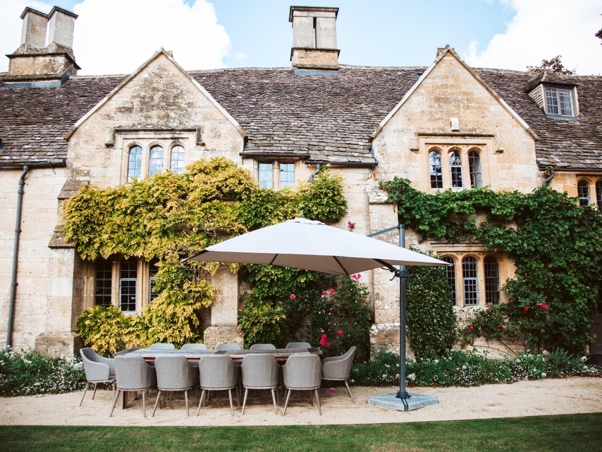 Shaded outdoor dining area in front of the ivy-covered Temple Guiting Manor, luxury villa in the Cotswolds, England