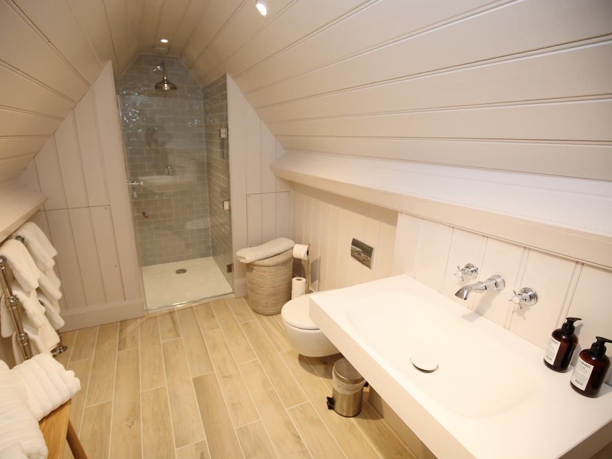 Bathroom with sink, toilet, laundry basket, towels and shower at Temple Guiting Manor in the Cotswolds, England