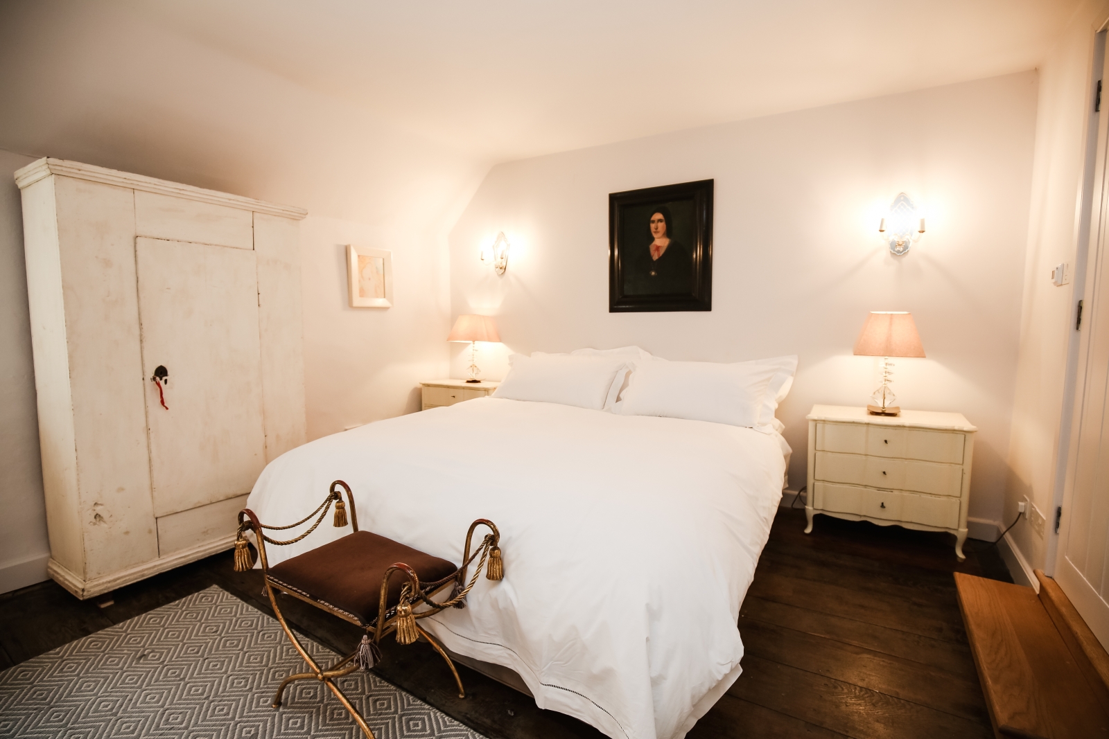 Bedroom with double bed, bedside tables, lamps, painting and wardrobe at Temple Guiting Manor in the Cotswolds, England