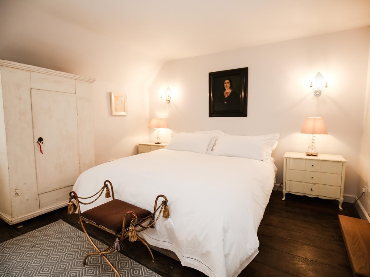 Bedroom with double bed, bedside tables, lamps, painting and wardrobe at Temple Guiting Manor in the Cotswolds, England