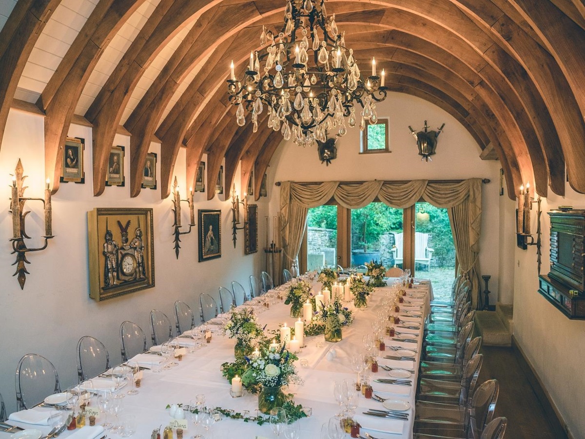 Dining room with set long table, chairs, paintings and chandelier at Temple Guiting Manor in the Cotswolds, England