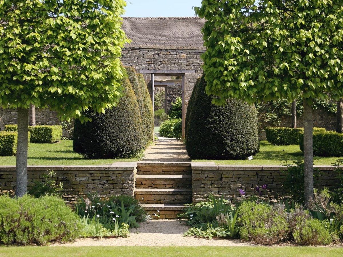Walled gardens with flowers, hedges, trees and steps at Temple Guiting Manor in the Cotswolds, England