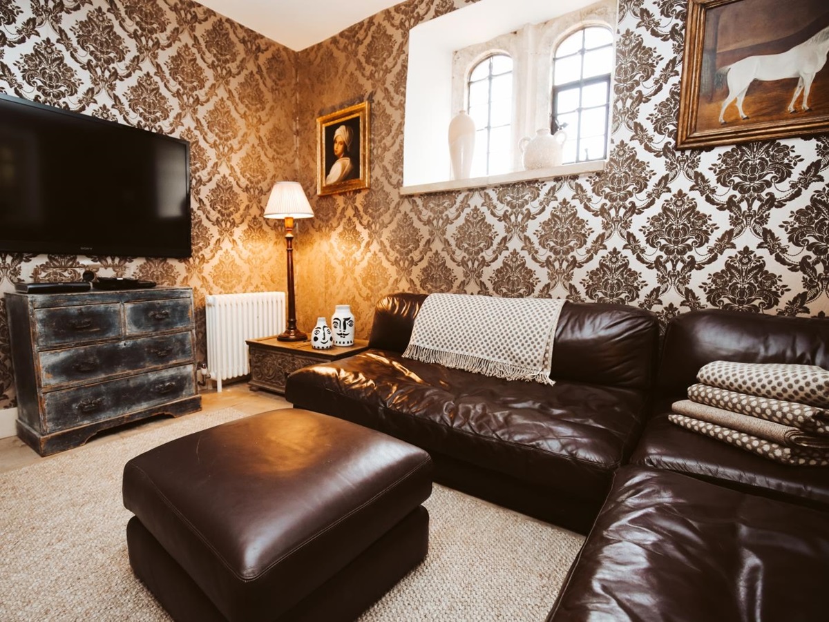 Lounge with long leather sofa, footstool, drawers, TV and paintings at Temple Guiting Manor in the Cotswolds, England
