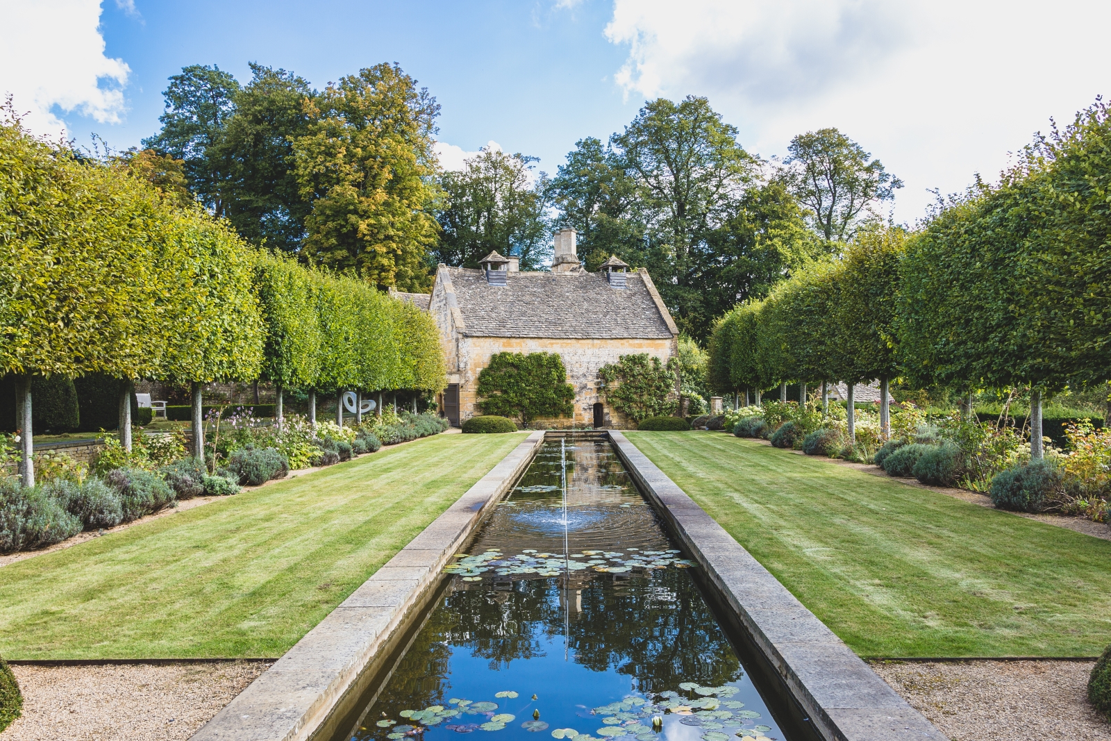 Water feature lined with trees leading to luxury villa Temple Guiting Manor in the Cotswolds
