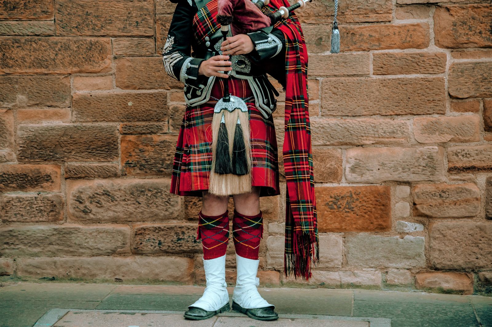A Scottish bagpiper in a kilt and traditional red tartan